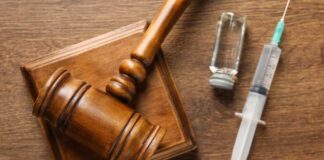 A wooden gavel next to a syringe and a vial on a wooden surface