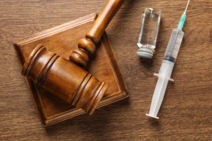 A wooden gavel next to a syringe and a vial on a wooden surface
