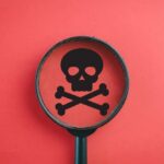 Magnifying glass focusing on a skull and crossbones symbol against a red background