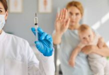 A healthcare professional holding a syringe while a mother with a baby shows a gesture of refusal