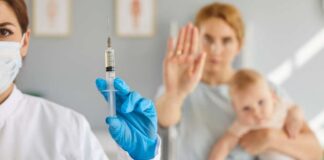 A healthcare professional holding a syringe while a mother with a baby shows a gesture of refusal