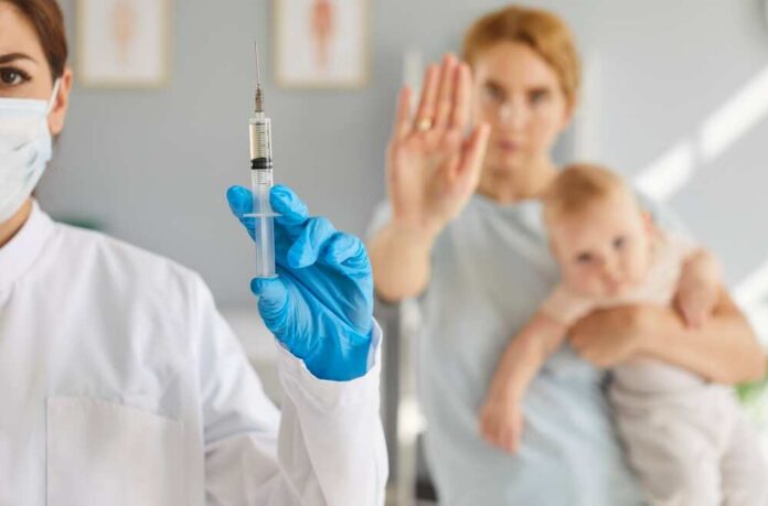 A healthcare professional holding a syringe while a mother with a baby shows a gesture of refusal