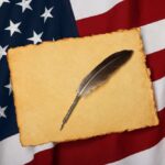 A quill pen resting on a blank parchment over an American flag