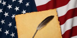 A quill pen resting on a blank parchment over an American flag
