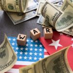Dollar bills surrounding wooden blocks spelling 'WAR' on flags of the USA and China