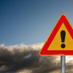 A triangular warning sign with an exclamation mark against a cloudy sky