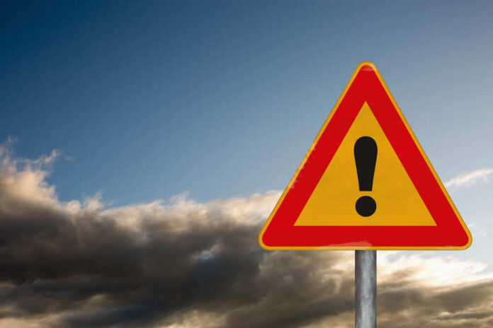 A triangular warning sign with an exclamation mark against a cloudy sky
