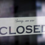 A sign hanging in a window that reads 'Sorry, we are CLOSED'