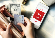 Person holding a credit card and cash while looking at a phone displaying debt information