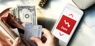 Person holding a credit card and cash while looking at a phone displaying debt information