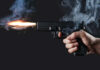A hand holding a gun with smoke and a flash from the muzzle