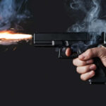 A hand holding a gun with smoke and a flash from the muzzle