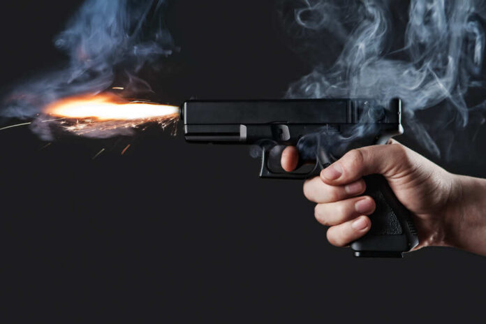 shutterstock_129133769.jpg A hand holding a gun with smoke and a flash from the muzzle