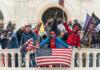 Group of people with flags outside a building balcony.