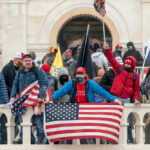 Group of people with flags outside a building balcony.