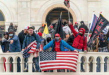 Group of people with flags outside a building balcony.