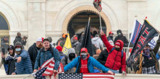 Group of people with flags outside a building balcony.