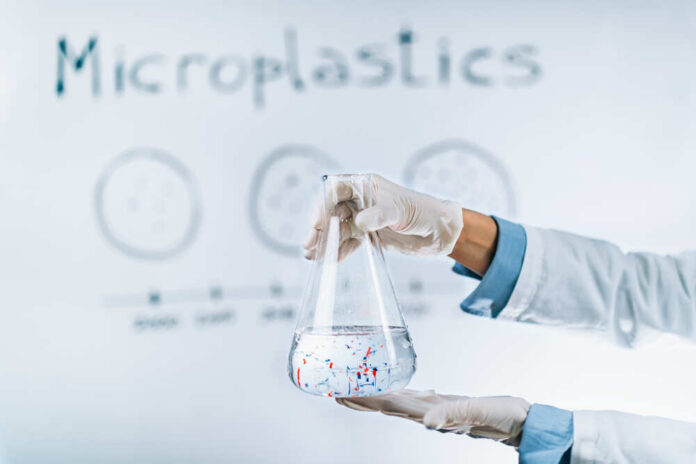 Scientist holding a flask containing water with microplastics in a laboratory setting