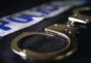 Close-up of handcuffs on a dark surface with police tape in the background