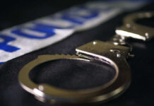 Close-up of handcuffs on a dark surface with police tape in the background