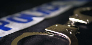 Close-up of handcuffs on a dark surface with police tape in the background