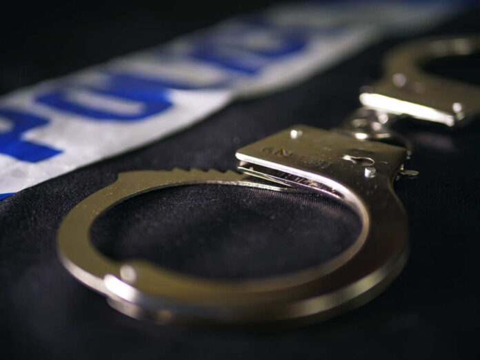 Close-up of handcuffs on a dark surface with police tape in the background