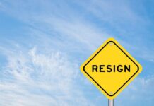A yellow warning sign with the word 'RESIGN' against a blue sky