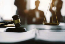 Gavel and scales in courtroom with blurred figures behind.