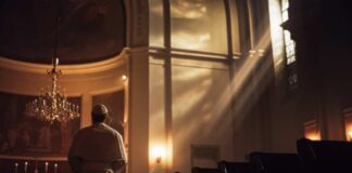 A clergy member standing in a church with light streaming through windows