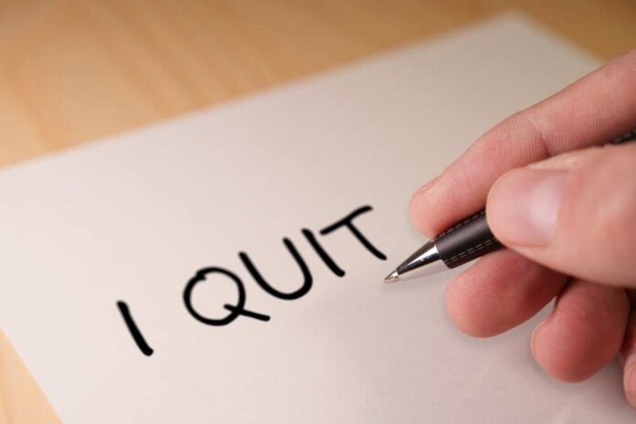 A hand writing 'I QUIT' on a piece of paper