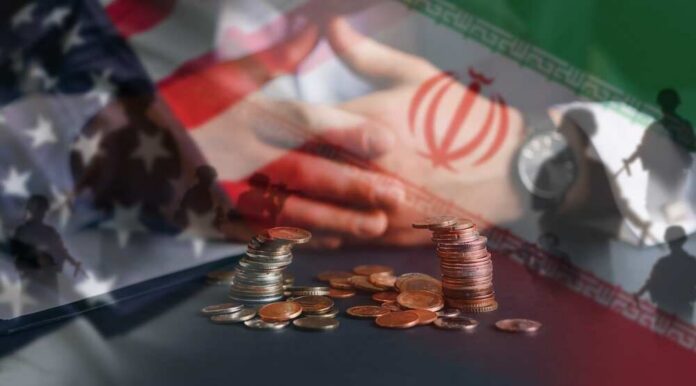 A hand resting on a table with coins stacked in front, overlaid with flags of the US and Iran