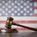 A wooden gavel resting on a sound block with an American flag background