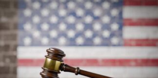 A wooden gavel resting on a sound block with an American flag background