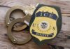 ICE officer badge next to handcuffs on a wooden surface