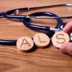 A hand holding wooden letters 'A', 'L', and 'S' next to a stethoscope on a wooden surface