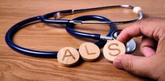 A hand holding wooden letters 'A', 'L', and 'S' next to a stethoscope on a wooden surface