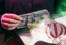A person holding a stack of US hundred-dollar bills in front of the Iranian flag