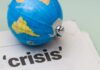 A small globe resting on a newspaper with the word 'crisis'