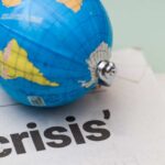A small globe resting on a newspaper with the word 'crisis'