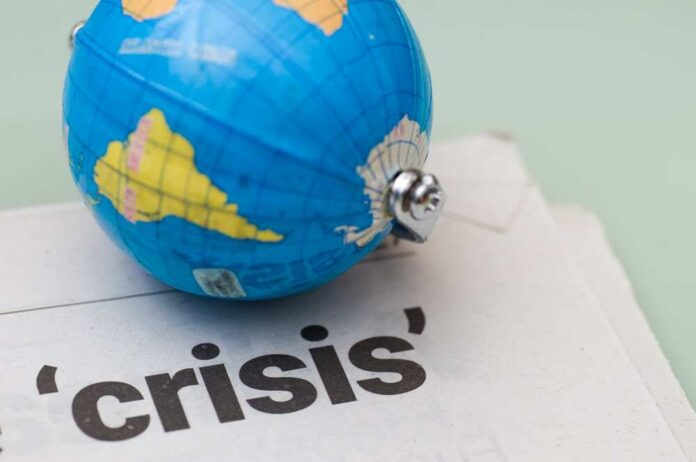 A small globe resting on a newspaper with the word 'crisis'