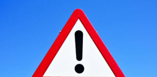 A triangular warning sign with an exclamation mark against a blue sky