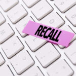 A pink sticky note with the word 'RECALL' placed on a white keyboard