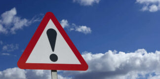 Warning sign with exclamation mark against sky