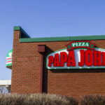 Papa John’s Pizza Box Sparks Viral Outrage Exterior view of a Papa John's pizza restaurant with a flag in the background