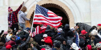 Crowd storming a building, waving an American flag.