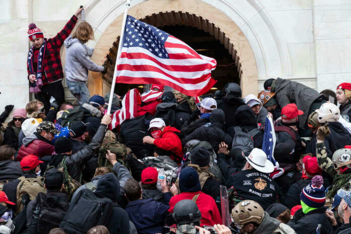 shutterstock_1889190787-1 Crowd storming a building, waving an American flag.