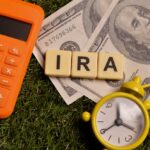 Calculator, dollar bills, and letter tiles spelling 'IRA' on grass