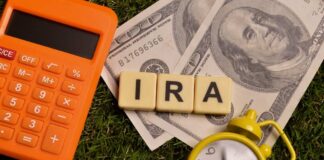 Calculator, dollar bills, and letter tiles spelling 'IRA' on grass
