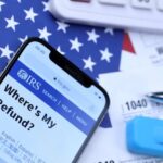 Smartphone displaying IRS website with tax documents and American flag in the background