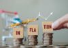 Hand pointing at blocks spelling 'INFLATION' on stacked coins with a shopping cart in the background
